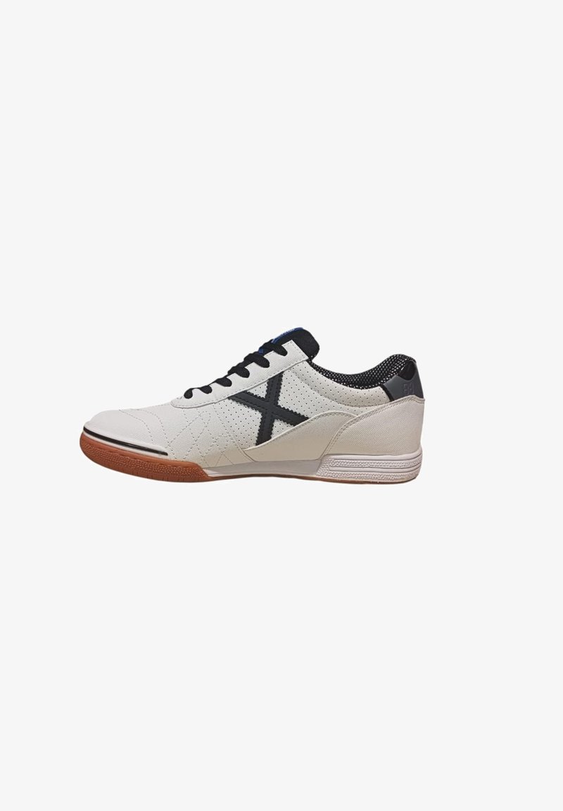 Zapatilla blanca con acentos negros, que presenta un diseño acolchado, lengüeta de malla y suela de goma. Incluye un prominente logotipo negro en forma de X.