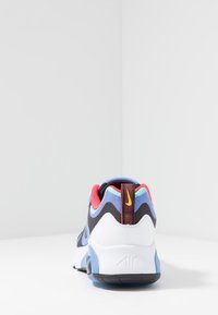 Buty sportowe Nike z czarną siateczkową cholewką z niebieskimi i różowymi akcentami, białą podeszwą środkową oraz teksturowanym obszarem pięty z żółtym logo.