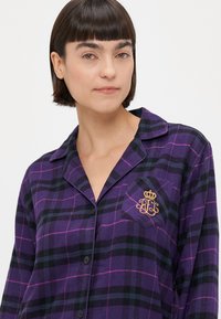 Μωβ καρό πουκάμισο με κουμπιά που διαθέτει τσέπη με χρυσή λεπτομέρεια στέμματος. Φτιαγμένο από απαλό ύφασμα με πράσινες και ροζ λωρίδες.