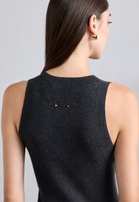 Ärmlös mörkgrå stickad topp med rund halsringning och subtil detalj på ryggen som har två små guldfärger. Slät textur, figurnära passform.