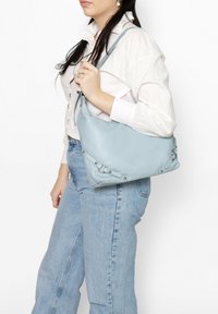 Borsa a tracolla in pelle azzurro chiaro con una texture liscia, caratterizzata da dettagli in metallo argentato e un design morbido.