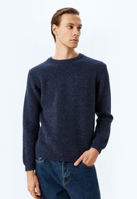 Marineblauer, gerippter Strickpullover mit gesprenkelter Textur, Rundhalsausschnitt, langen Ärmeln und lässiger Passform, kombiniert mit lockeren Jeans.