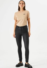 Camiseta de algodón beige con un pequeño dise�ño gráfico, combinada con jeans de mezclilla ajustados negros. El conjunto se complementa con zapatos negros.