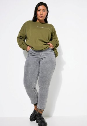 Olivově zelená mikina s nápisem "WEEKEND VIBES", v kombinaci se světle šedými slim fit džíny a černými robustními mokasíny, na bílém pozadí.