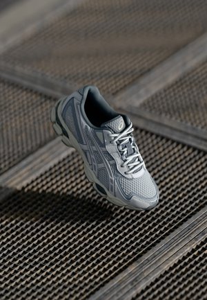 Gray and white athletic sneaker with mesh and synthetic upper, laces tied, positioned above a textured metal surface.