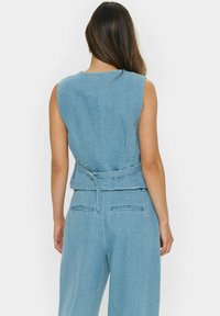 Modra jeansova kombinezon z oprijetim telesom, širokimi hlačami in pasom. Ima brezrokavni dizajn in diskretne šive.