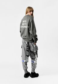 Sudadera gris de gran tamaño con el texto "MOD WAVE OVEMNT", combinada con pantalones cargo grises claros que cuentan con múltiples bolsillos y correas. Calzado negro.