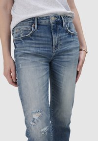 Jasnoniebieskie jeansy z przetartym denimu, ze strzępionymi detalami na kolanach, w dopasowanym kroju, pięć kieszeni, z subtelnymi przetarciami dla uzyskania zużytego wyglądu.