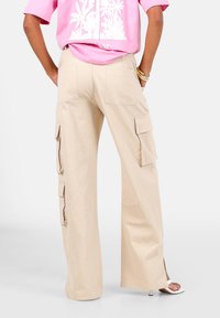 Beige wijdvallende cargo broek met twee zijzakken, twee achterzakken en een gladde textuur, gecombineerd met een roze cropped shirt.