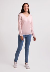 Ljust rosa, långärmad stickad tröja med V-ringning. Bärs med blå, slim-fit jeans och vita sneakers. Slät textur, avslappnad stil.
