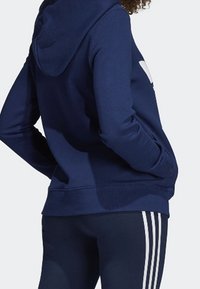 Navy- värinen huppari, joka on valmistettu puuvillasekoitteesta. Siinä on kengurupocket, ribattuja hihansuita ja suuri valkoinen logo selässä.