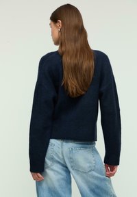 Navy blue knitted sweater with dropped shoulders, ribbed hem, and long sleeves, paired with light blue high-waisted jeans.