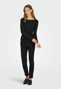 Zwarte lange mouw top met een bateauhals, gecombineerd met slim-fit zwarte jeans. De outfit heeft een gladde, textuurstof en platte zwarte schoenen.