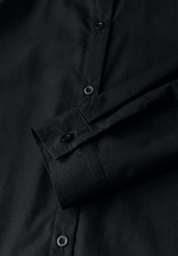 Camicia nera a maniche lunghe con bottoni frontali visibili e un bottone sul polsino, distesa piatta con la manica piegata sopra il corpo.