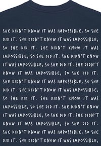 T-shirt bleu marine avec un texte blanc répété disant : "Elle ne savait pas que c'était impossible, alors elle l'a fait", dans une police décontractée.