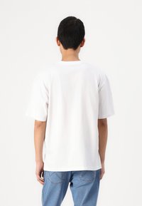 White cotton t-shirt with short sleeves, a crew neck, and a relaxed fit, paired with light blue denim jeans. Minimalist design, no patterns.