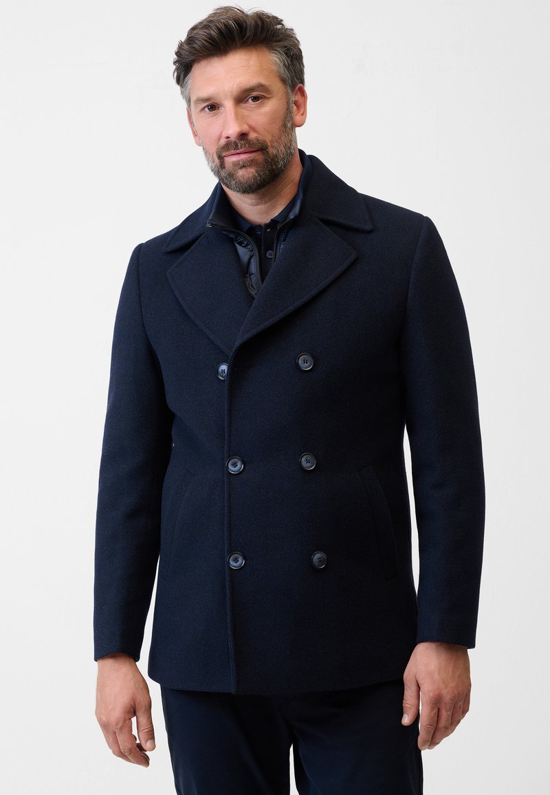 Marineblauer, doppelt geknöpfter Wollmantel mit Reverskragen, großen Knöpfen, Klappentaschen und einer strukturierten Oberfläche.