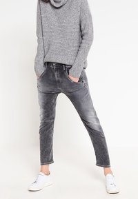 Gray jeans with a faded texture and tapered cut, paired with a loose-knit gray sweater and white sneakers.