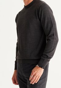 Dunkelgrauer Strickpullover mit Rundhalsausschnitt, gerippten Bündchen und Saum. Der Stoff wirkt weich und leicht strukturiert, figurbetonte Silhouette.