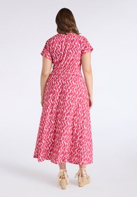 Pink dress with an abstract zigzag pattern, short sleeves, and a cinched waist. Floor-length with a flowing silhouette and paired with wedge sandals.