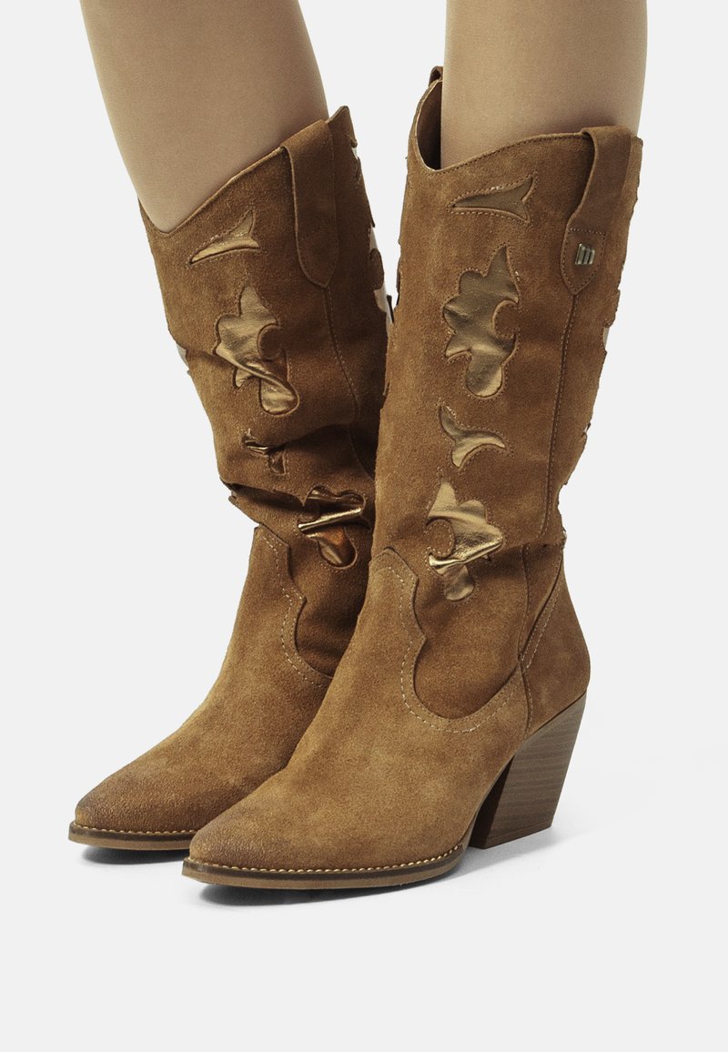 Botas de vaquero de ante marrón con punta afilada, recortes decorativos y tacón apilado. Presenta detalles en dorado y costuras decorativas.