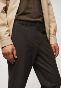 Czarne spodnie o gładkiej fakturze, z dopasowanym krojem, bocznymi kieszeniami oraz paskiem biodrowym z szlufkami, zestawione z beżową kurtką.