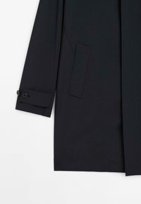 Sort frakke med et lige design, der har en sidelomme, knapmanchetter og en glat, mat tekstur. Skabt til et rent udseende.
