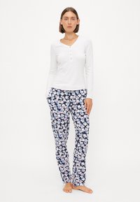 Haut henley blanc à manches longues avec trois boutons et pantalon de pyjama floral bleu marine, orné de fleurs roses et blanches sur un fond sombre.