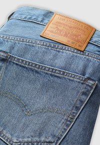 Poche arrière d’un jean Levi’s 501 bleu clair avec une étiquette de marque en cuir marron indiquant la taille W 32 L 32 et les détails des coutures.