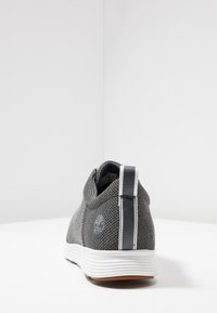 Šedá textilní teniska s hladkým povrchem, bílou podrážkou, pruhovaným akcentem na patě a detailem loga na boku.