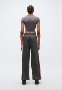 Szürke, testhez simuló rövid ujjú felső, laza fekete tréningnadrággal, melyen rózsaszín oldalsávok és patentgombos részletek találhatók.