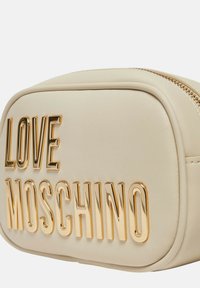 Borsa in similpelle beige dalla forma arrotondata, con logo dorato "LOVE MOSCHINO" impresso sul davanti e chiusura con zip.
