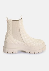 Bottine beige en cuir matelassé avec semelle épaisse à crampons, panneau latéral élastique et languettes à l'avant et à l'arrière.