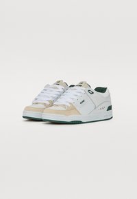 White and tan sneakers with green accents. Materials include smooth leather and textured suede. Features includes flat white laces and a padded collar.