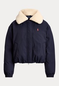 Veste matelassée bleu marine avec col sherpa crème, manches longues, poignets élastiques, fermeture éclair à l'avant et petit logo rouge sur la poitrine.