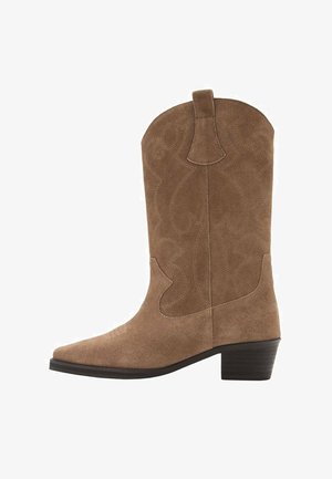 Bottes western en daim marron avec un bout pointu, des coutures décoratives, une tige haute et un talon empilé. Dotées d'une languette de tirage au sommet.