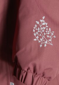 Rosa jackärm med en strukturerad herringbone-mönster, prydd med vit blommig broderi och en rynkad manschettdetalj.