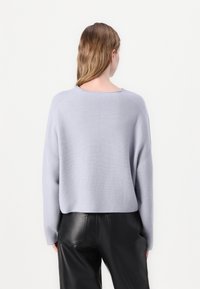 Hellgrauer, kurzer Pullover mit weitem Ausschnitt und langen Ärmeln, kombiniert mit glänzenden schwarzen Lederhosen. Weiche Textur, minimalistisches Design.