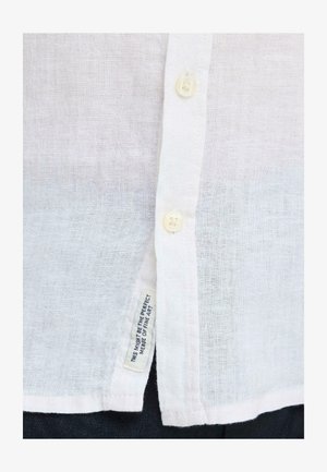 Valge tekstuuriga särgi eesosa, millel on kaks valget nuppu ja kangasmärgiga silt, millel on kirjas "See võib olla täiuslik peenearsti ühendus."