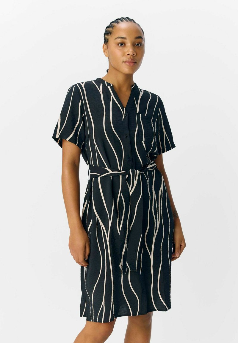 Robe à manches courtes, longueur genou, en noir avec des rayures ondulées blanches. Dotée d'une fermeture à boutons sur le devant, d'un col et d'une ceinture assortie à la taille.