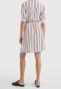 Vit klänning med vertikala ränder i rött och svart. Korta ärmar, krage och tight midja. Slätt tyg med en lätt känsla.