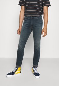 Mörkblå slim-fit jeans med lätt blekning, matchade med en svart och vit randig skjorta samt klara blå och gula högklackade sneakers.