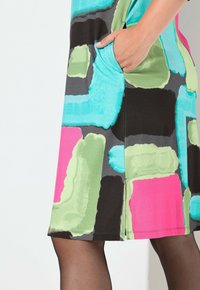 Värikäs hihaton mekko, jossa on kuvio valkoisia, vihreitä, pinkkejä ja mustia muotoja. Sisältää sivutaskun ja pehmeän pinnan.