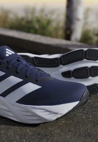 Pair of blue and white running shoes with black rubber soles placed on outdoor pavement near a curb.