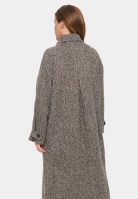 Cappotto grigio a spina di pesce con colletto, caratterizzato da un design lungo e fluido e maniche con bottoni. Il tessuto testurizzato aggiunge interesse visivo.