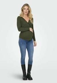 Oliivroheline ribadega pikkade varrukatega topp V-kaelusega ja pitsäärisega, koos heledate siniste teksade ja mustade üliõhukeste saapetega.