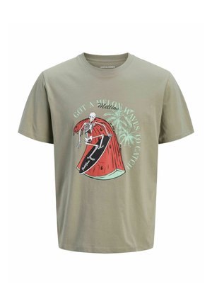 Smilende dreng iført lysegrå grafisk t-shirt, denimshorts, hvide sokker og beige sko, der står foran en simpel hvid baggrund.