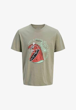 Niño sonriente que lleva una camiseta gráfica de color gris claro, pantalones cortos vaqueros, calcetines blancos y zapatos beige, de pie sobre un fondo blanco liso.