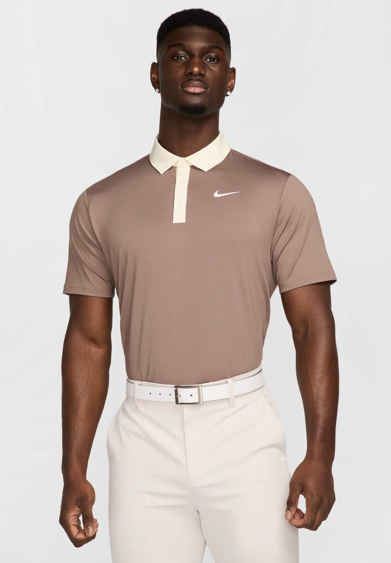 Brūns īsām piedurknēm polo krekls ar krēmkrāsas apkakli, ar mazu baltu Nike logo. Saskaņots ar baltām biksēm un baltu jostu.