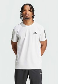 T-shirt atlética branca de mangas curtas, com detalhes em três riscas pretas nas mangas e um pequeno logótipo preto no peito.